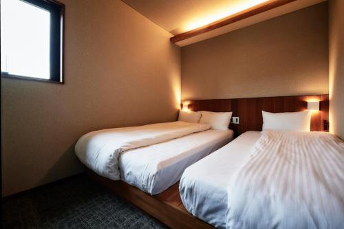 two beds in a small room with a window at &HOTEL HAKATA in Fukuoka