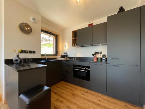 une cuisine avec des placards gris et une horloge murale dans l'établissement Homency - Résidence Chalets du Golf - Birdy B202, à L'Alpe-d'Huez