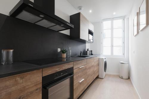 - une cuisine avec des placards noirs et en bois et une cuisinière dans l'établissement OIQIA • Arthéa • Esquisse, à Périgueux