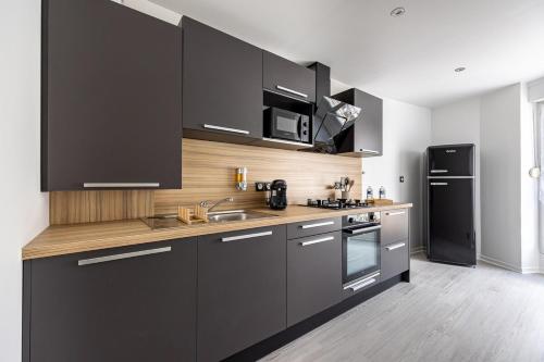 La cuisine est équipée de placards noirs, d'un évier et d'un réfrigérateur. dans l'établissement OIQIA • Téralis • Estival, à Annonay