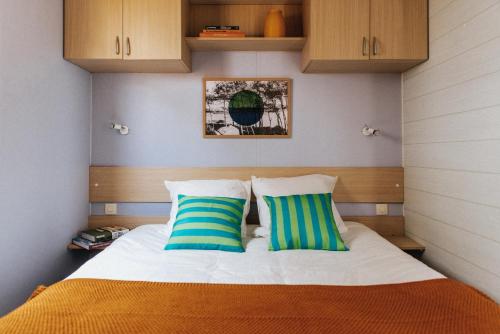 une chambre avec un lit avec deux oreillers bleus et verts dans l'établissement Camping Liberté Landrellec, à Pleumeur-Bodou