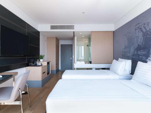 a bedroom with two beds and a desk and a tv at Novotel Phnom Penh BKK 1 in Phnom Penh