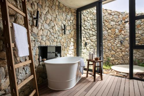 a bathroom with a tub and a stone wall at Fifty-Five Mjejane in Hectorspruit