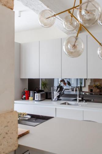 La cuisine est équipée de placards blancs, d'un évier et de lumières. dans l'établissement 196 Suite Dan - Superbe Appartement à Paris, à Paris
