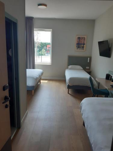a room with two beds and a desk and a window at Kyriad Limoges - Ester in Limoges