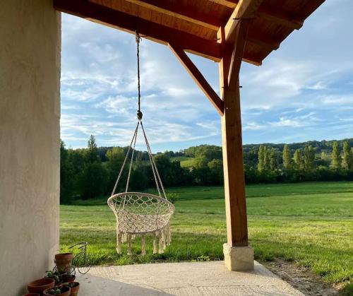 a chair hanging from a porch with a view of a field at Maison de charme à la campagne in Montpezat