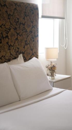 a bed with white sheets and a wall with a window at El Golf Hotel Boutique in Lima