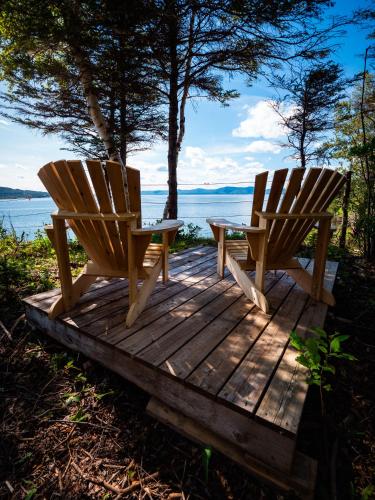 two wooden chairs sitting on a wooden deck near the water at ÈST Éco-cabines in Nouvelle