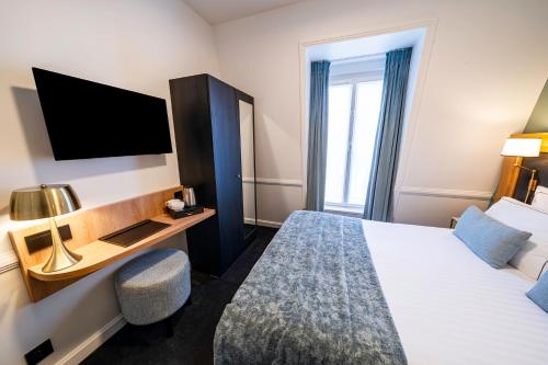 a hotel room with a bed and a desk and a tv at Hôtel Le Cercle Tour Eiffel in Paris