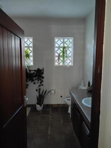 a bathroom with a sink and a toilet and two windows at Diani Beach Cottage Apartment in Ukunda