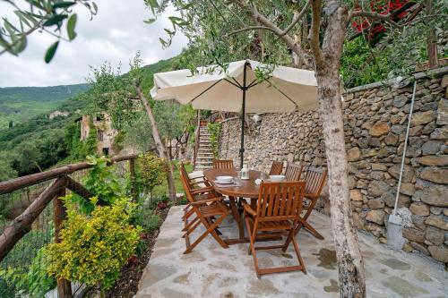 a table and chairs with an umbrella on a stone wall at Agriturismo U' Spigu Nonna Annetta in Nasino