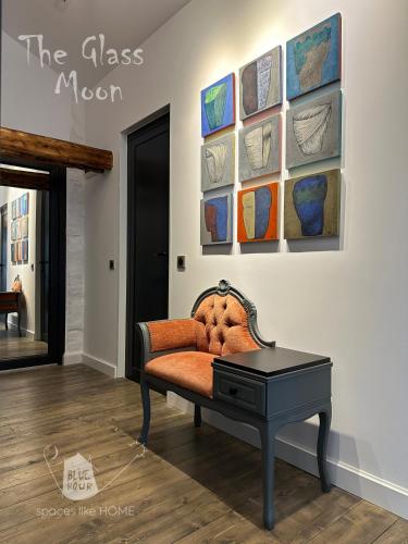 a room with a chair and a table and paintings on the wall at Пространства за гости Синият час - апартамент The Glass Moon in Ruse