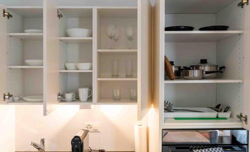 a kitchen with white shelves with dishes and glasses at Los Lorentes Apartments Bern Airport in Belp