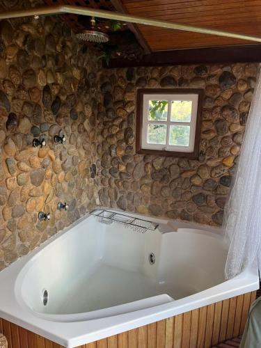 a bath tub in a room with a stone wall at Chalés do Cachoeirão in Visconde De Maua