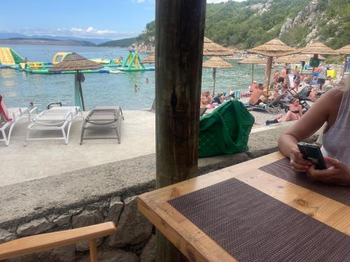a woman sitting at a table in front of a beach at Lux dodo in Dramalj