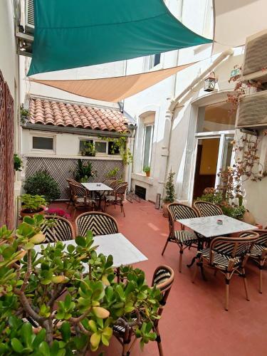 un patio extérieur avec des tables, des chaises et un parasol vert dans l'établissement Hotel de France, à Narbonne