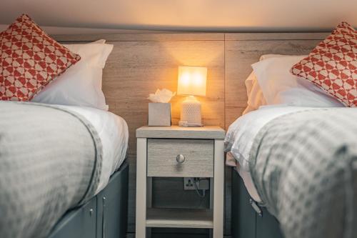 two beds with a night stand with a lamp on it at Rooms at the Apple Pie in Ambleside