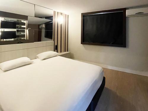 a bedroom with a white bed and a television at Villages Motel by Drops in Lages