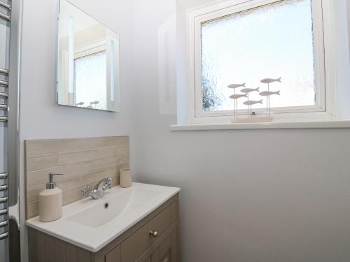 a bathroom with a sink and a mirror and a window at Llwyn Eithin in Benllech