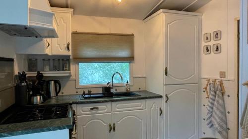 a kitchen with white cabinets and a sink and a window at SAYANG26 gezellige gezinsvriendelijke stacaravan op familiecamping De Vossenburcht in natuurgebied Reestdal - no workers allowed in IJhorst