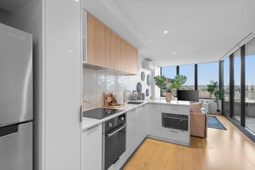 a kitchen with white appliances and large windows at Complete Host STK Apartments in Melbourne