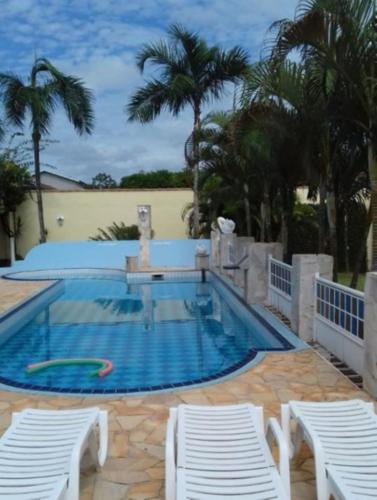 a large swimming pool with two white chairs and palm trees at Recanto Serenissima in São Pedro