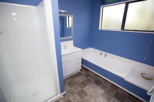La salle de bains est pourvue de murs bleus, d'une baignoire et d'un lavabo. dans l'établissement The Coast Motel, à Timaru
