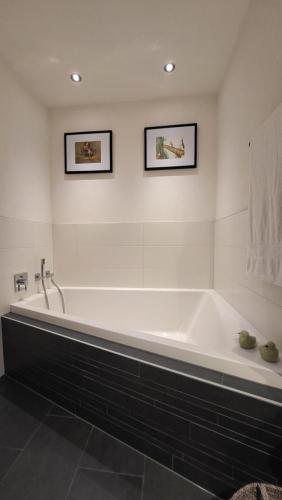 a white bathroom with a tub and two pictures on the wall at Chasa Scandella Apartment Tanja in Sent