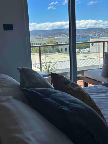 a room with a bed with pillows and a large window at City fringe modern apartment with car parking in Hobart