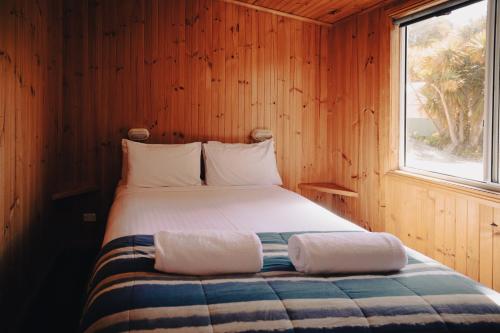 a bed in a wooden room with a window at Strahan Beach Tourist Park in Strahan