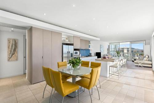 a kitchen and living room with a table and yellow chairs at Azure Bliss - Majestic Apartment on the Water in Safety Beach
