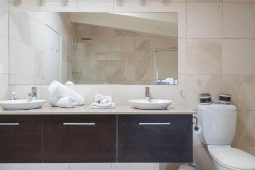 a bathroom with a toilet and two sinks and a mirror at Port Philip Panorama - Bayview Retreat and Pool Bliss in Mount Martha