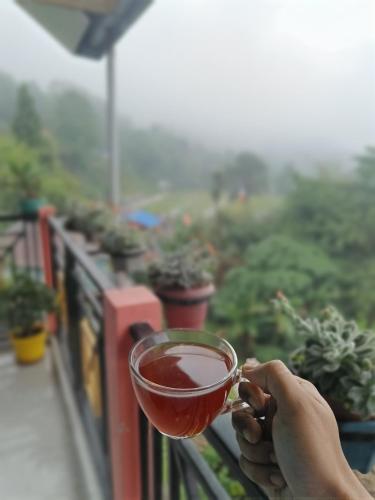 a person holding a cup of tea on a balcony at Sotang Homestay Ramdhura in Kalimpong
