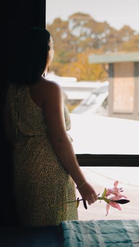 a woman holding a flower in front of a window at Strahan Beach Tourist Park in Strahan
