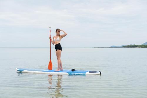 a woman standing on a paddle board in the water at The Briza Beach Resort, Samui - SHA Plus in Chaweng