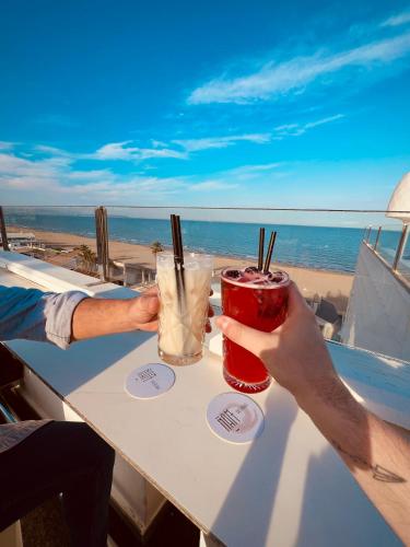 two people holding drinks at a table near the beach at Hotel Meridional in Guardamar del Segura