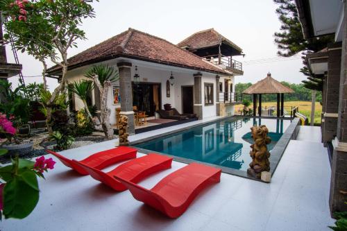 a villa with a swimming pool and red chairs at Balam Bali Villa in Mengwi