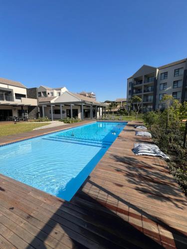 a swimming pool with a wooden deck and buildings at Ballito Village Suites in Ballito