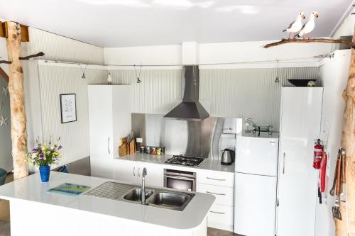 una cucina bianca con lavandino e frigorifero di Larus Waterfront Cottage a White Beach