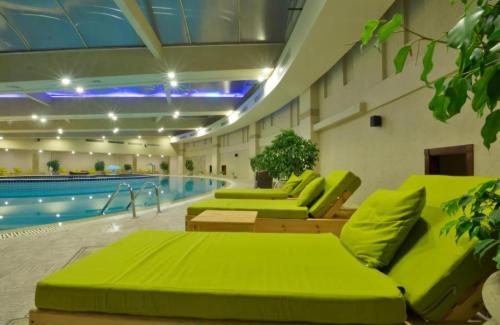 a pool room with green furniture and a swimming pool at فندق بورتو مارينا - غرفة فندقية بخدمة فندقية in El Alamein