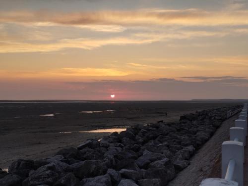 a sunset over a beach with a rock wall at L'intemporelle in Le Crotoy