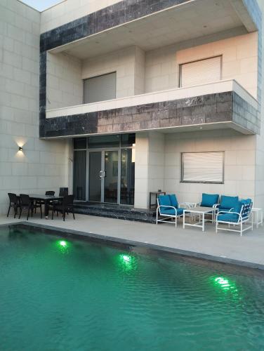 a house with a swimming pool with chairs and a table at Airport chalet amman in Al Qasţal
