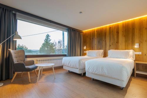 a hotel room with two beds and a chair and a window at La Mira de Gredos in Hoyos del Espino