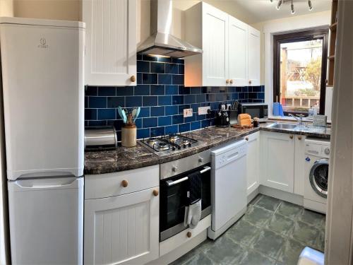 una cocina con armarios blancos y azulejos azules en Aultnagar, en Kirkton of Largo