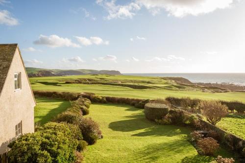 une vue sur un terrain de golf avec une maison et l'océan dans l'établissement Beachside, Luxury Cottage, Devon, à Thurlestone