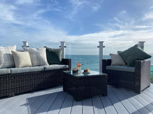 a patio with two wicker chairs and a table and the ocean at Swift Mosselle Pitch 24 Creek Caravan Park dog friendly in Ringstead