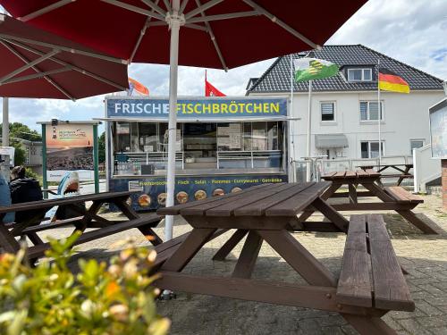 two picnic tables with an umbrella in front of a restaurant at Mertinkus Nordseehotel in Cuxhaven