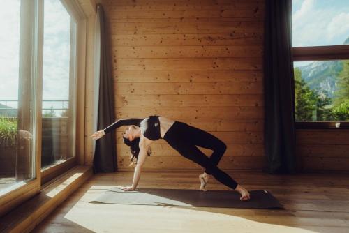 a woman doing a yoga pose in a room with a window at Holzhotel Forsthofalm in Leogang