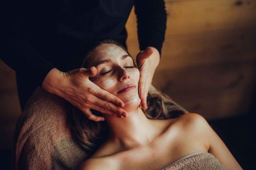 a woman getting her face moisturized by a massage therapist at Holzhotel Forsthofalm in Leogang