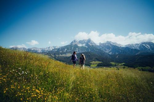 two people walking on a hill with mountains in the background at Holzhotel Forsthofalm in Leogang